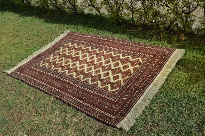 May include: A traditional rug with a geometric pattern in shades of red, white, and brown. The rug has a fringe border and is laid out on a green grassy surface.