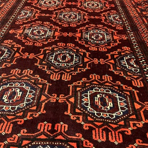 May include: Close-up of a dark red rug with a repeating geometric pattern. The design features orange, white, and navy blue accents. The rug's intricate pattern and rich colour palette create a warm, inviting aesthetic.