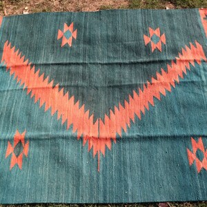 May include: A teal and orange patterned rug with a geometric design. The rug has a fringe border and is made of woven fabric.