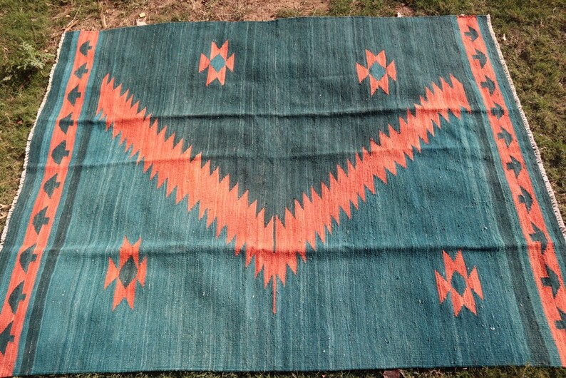 May include: A teal and orange patterned rug with a geometric design. The rug has a fringe border and is made of woven fabric.