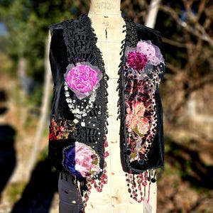 K&ouml;nnte beinhalten: Schwarze Samtweste mit floralen Applikationen, Spitzenbesatz und Perlenfransen. Mit rosa und lila Stoffblumen, Pailletten und h&auml;ngenden Perlen verziert. Gezeigt auf einer Vintage-Schneiderpuppe.