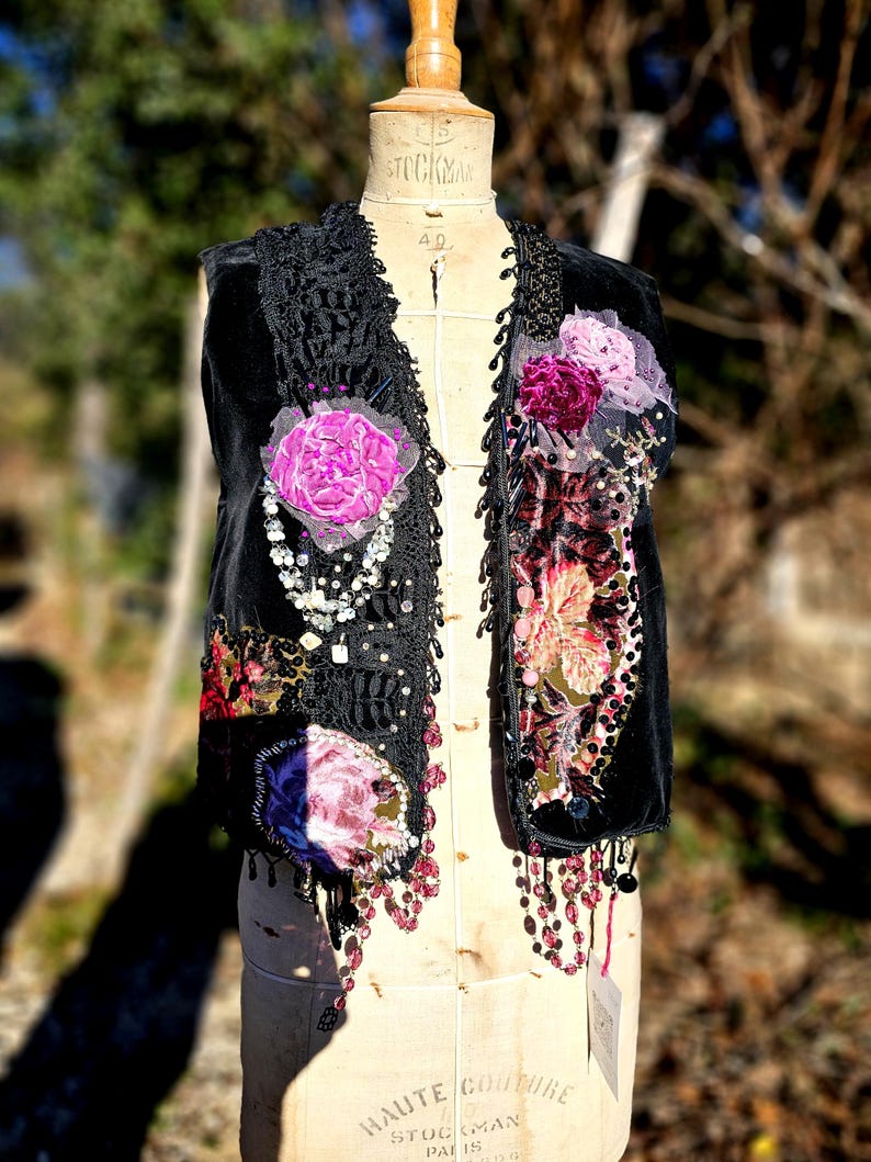 K&ouml;nnte beinhalten: Schwarze Samtweste mit floralen Applikationen, Spitzenbesatz und Perlenfransen. Mit rosa und lila Stoffblumen, Pailletten und h&auml;ngenden Perlen verziert. Gezeigt auf einer Vintage-Schneiderpuppe.