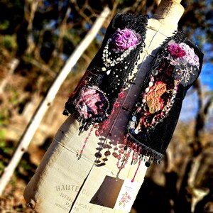 K&ouml;nnte beinhalten: Eine schwarze Weste mit floralen Verzierungen, Perlen und Spitze, pr&auml;sentiert auf einer Vintage-Schneiderpuppe. Die Weste hat lila und rosa Blumen mit herabh&auml;ngenden Perlenakzenten. Die Schneiderpuppe tr&auml;gt den Text "HAUTE COUTURE STOLKMAN PARIS BREVETE".