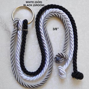 May include: Three 3/8 inch thick twisted ropes in silver gray, white, and black, each attached to a single silver metal ring. The ropes are labeled as SILVER GRAY (BRIDE), WHITE (GOD), and BLACK (GROOM) with knotted ends at the bottom.