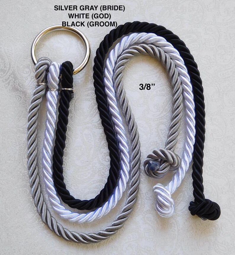 May include: Three 3/8 inch thick twisted ropes in silver gray, white, and black, each attached to a single silver metal ring. The ropes are labeled as SILVER GRAY (BRIDE), WHITE (GOD), and BLACK (GROOM) with knotted ends at the bottom.