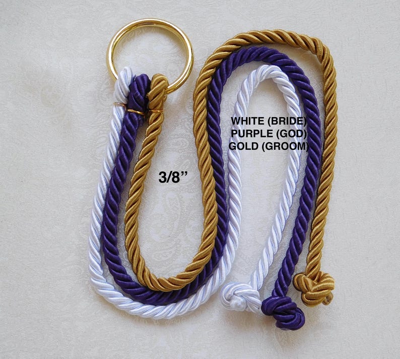 Peut inclure: Un ensemble de trois cordes torsad&eacute;es blanches, violettes et dor&eacute;es, d'un diam&egrave;tre de 3/8 pouces, fix&eacute;es &agrave; un anneau m&eacute;tallique dor&eacute;. Les cordes pr&eacute;sentent des n&oelig;uds aux extr&eacute;mit&eacute;s et le texte : WHITE (BRIDE), PURPLE (GOD), GOLD (GROOM).