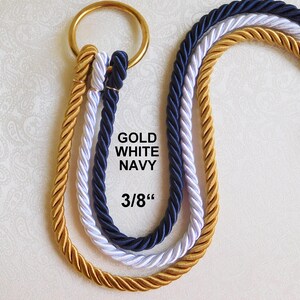 Peut inclure: Trois cordes torsad&eacute;es de couleur or, blanc et bleu marine, chacune pass&eacute;e dans un anneau m&eacute;tallique dor&eacute;. Le texte GOLD WHITE NAVY et 3/8" est imprim&eacute; en noir au centre des cordes, indiquant le diam&egrave;tre de la corde.