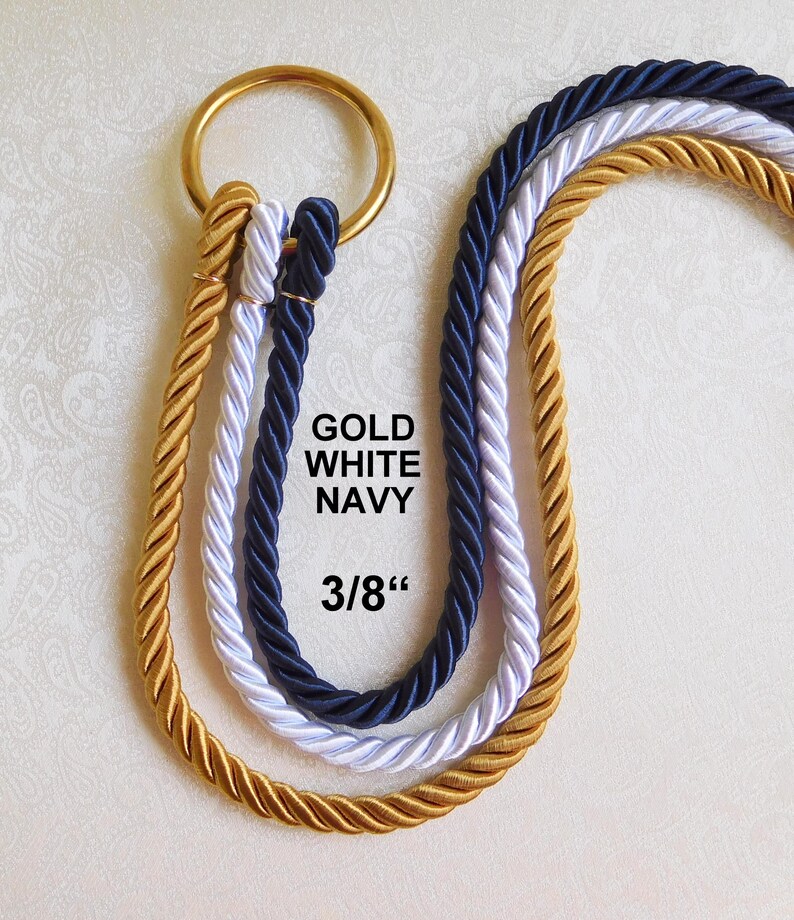 Peut inclure: Trois cordes torsad&eacute;es de couleur or, blanc et bleu marine, chacune pass&eacute;e dans un anneau m&eacute;tallique dor&eacute;. Le texte GOLD WHITE NAVY et 3/8" est imprim&eacute; en noir au centre des cordes, indiquant le diam&egrave;tre de la corde.