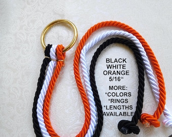 May include: Three twisted ropes in black, white, and orange are looped through a gold-toned metal ring. The text on the image reads: BLACK WHITE ORANGE 5/16" MORE: *COLORS *RINGS *LENGTHS AVAILABLE. The ropes have knotted ends.