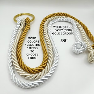 Op de afbeelding: Drie strengen touw, wit, ivoor en goud, zijn aan elkaar gebonden met een gouden ring. Het touw is 3/8 inch dik. De tekst op de afbeelding luidt: "MORE: * COLORS * LENGTHS * RINGS TO CHOOSE FROM WHITE (BRIDE) IVORY (GOD) GOLD (GROOM) 3/8""
