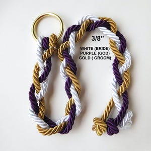 Peut inclure: Une corde tress&eacute;e compos&eacute;e de trois brins de couleur blanche, violette et dor&eacute;e, fix&eacute;e &agrave; un anneau en m&eacute;tal dor&eacute;. Le texte 3/8&rdquo;, WHITE (BRIDE), PURPLE (GOD), GOLD (GROOM) est imprim&eacute; sur l'image, indiquant un diam&egrave;tre de 3/8 de pouce.