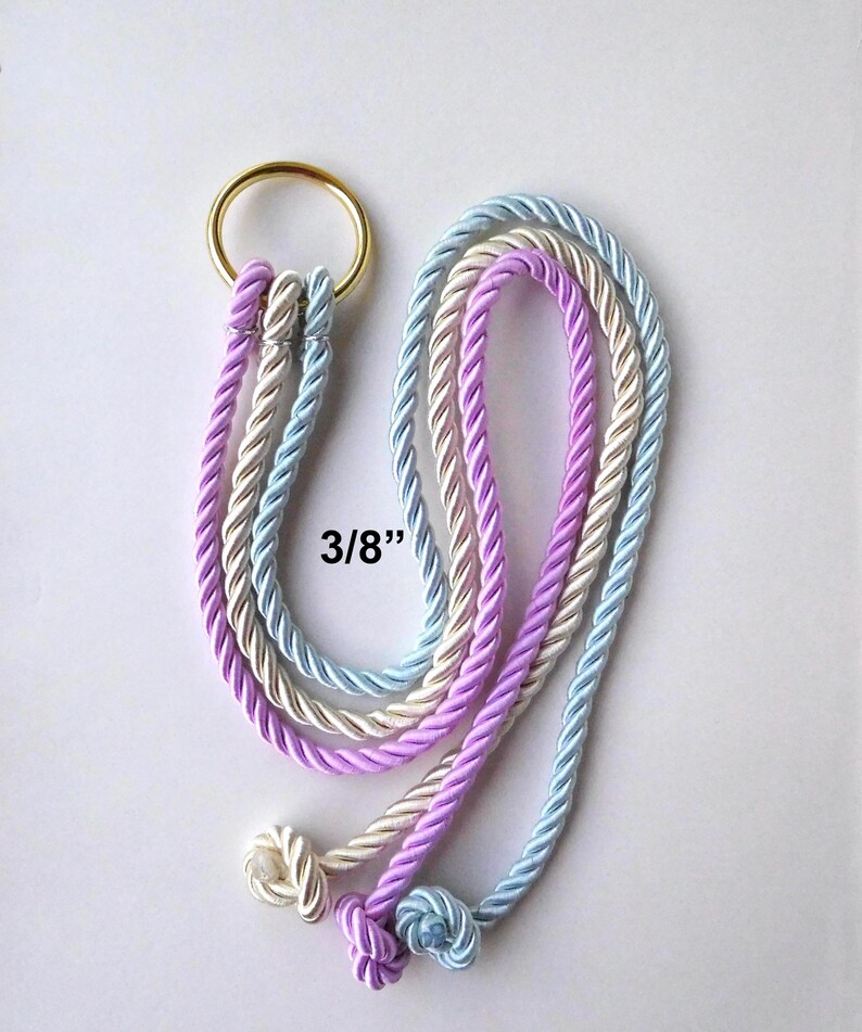 Peut inclure: Un anneau en m&eacute;tal dor&eacute; attach&eacute; &agrave; trois cordes torsad&eacute;es de couleur bleu clair, cr&egrave;me et lavande. Chaque corde pr&eacute;sente une extr&eacute;mit&eacute; nou&eacute;e et le texte 3/8" est imprim&eacute; pr&egrave;s du centre, indiquant le diam&egrave;tre de la corde pour cet objet.