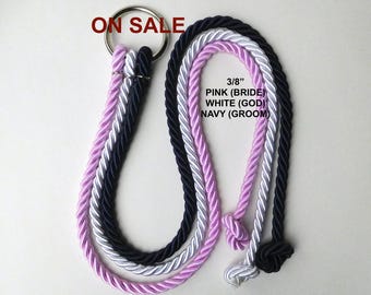 May include: Three 3/8 inch thick twisted ropes in pink, white, and navy blue attached to a silver metal ring. The ropes feature knots at the ends. Text on the image reads ON SALE, 3/8 PINK (BRIDE), WHITE (GOD), and NAVY (GROOM).