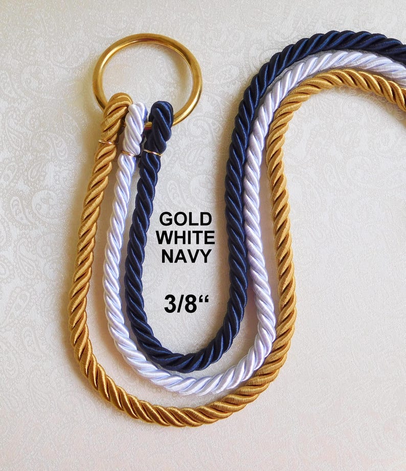 May include: Three twisted ropes in gold, white, and navy blue, each looped through a circular gold metal ring. The text GOLD WHITE NAVY and 3/8" is printed in black in the center of the ropes, indicating the rope diameter.
