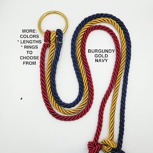 May include: Three twisted ropes in burgundy, gold, and navy blue attached to a gold metal ring. Text on the left reads: MORE: COLORS * LENGTHS * RINGS TO CHOOSE FROM. Text on the right reads: BURGUNDY GOLD NAVY. The ropes hang down in loops.