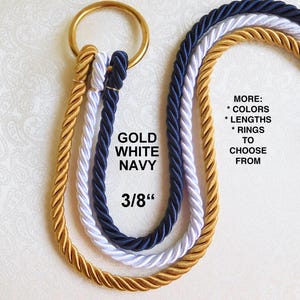 Op de afbeelding: Drie gevlochten koorden in goud, wit en marineblauw, gebonden met een gouden metalen ring. De koorden zijn 3/8 inch dik. De tekst "MORE: * COLORS * LENGTHS * RINGS TO CHOOSE FROM" is zichtbaar in de afbeelding.