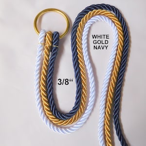 Op de afbeelding: Drie strengen touw, wit, goud en marineblauw, zijn aan elkaar gebonden met een gouden ring. Het touw is 3/8 inch dik en de kleuren zijn gelabeld met "WHITE GOLD NAVY".