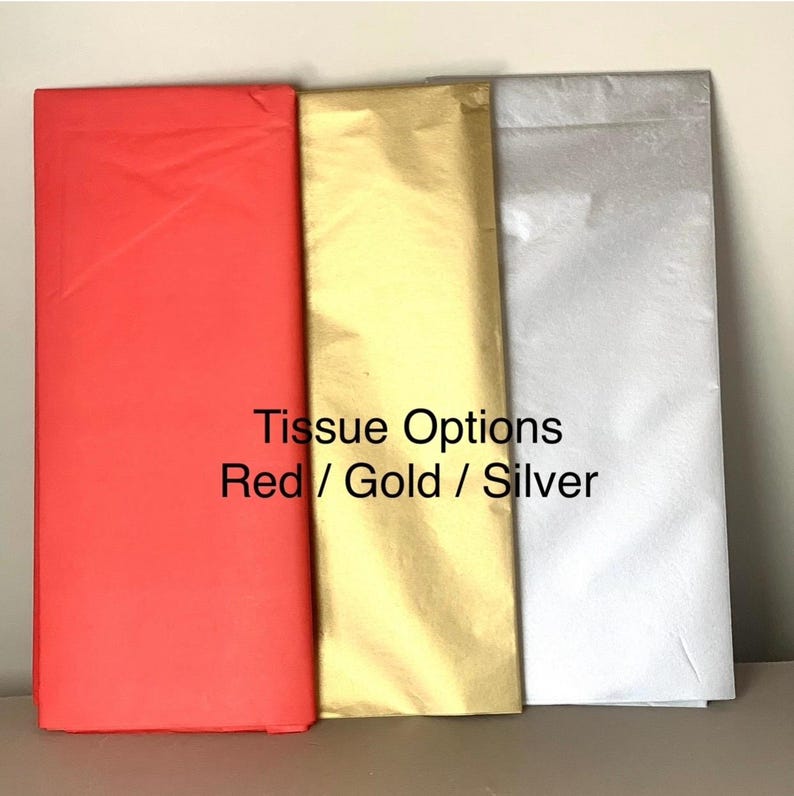 May include: Three rectangular sheets of tissue paper in red, gold, and silver. The text "Tissue Options Red / Gold / Silver" is printed on the image. The tissue paper is neatly folded and stacked, showcasing the color variations.