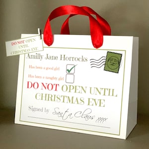 May include: A white gift bag with red ribbon handles and a tag that reads "Do Not Open Until Christmas Eve." The bag features text including "Amilly Jane Horrocks" and "Signed by Santa Claus."