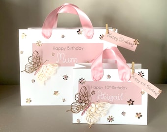 May include: Two white gift bags with pink ribbon handles and decorative butterflies. One bag reads "Happy Birthday Mum," the other says "Happy 10th Birthday Abigail." Both have tags that say "Happy Birthday."