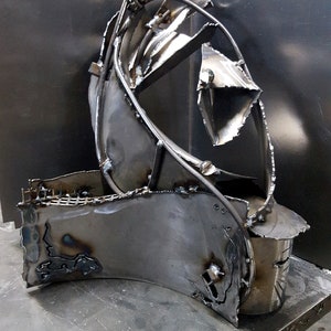 May include: A silver metal sculpture made of welded pieces of metal. The sculpture is abstract and has a flowing, organic shape.