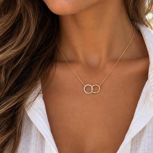 May include: A delicate necklace featuring two small, interlocking circular rings suspended from a thin chain. One ring is finished in a bright silver tone, while the other is finished in a warm gold tone, creating a subtle two-tone metallic effect.