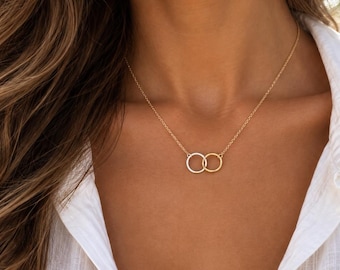May include: A delicate necklace featuring two small, interlocking circular rings suspended from a thin chain. One ring is finished in a bright silver tone, while the other is finished in a warm gold tone, creating a subtle two-tone metallic effect.