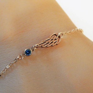 Guardian angel wing charm bracelet with personalized september birthstone option in gold filled chain is worn on a model for Gilded Sapphire's custom jewelry.