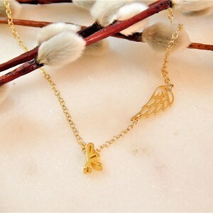 Puede incluir: Un collar de cadena dorada con un peque&ntilde;o dije de ala dorada y un dije de letra K dorada.