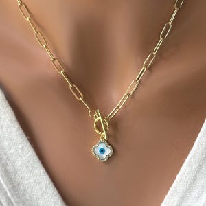 May include: Gold chain necklace with a toggle clasp and a white clover charm with a blue evil eye in the center.