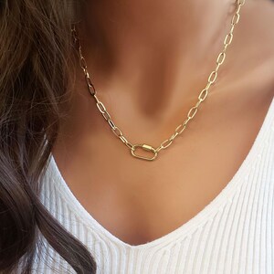 Puede incluir: Un collar de cadena dorada con un cierre ovalado dorado. El collar est&aacute; en un maniqu&iacute; que lleva una camisa blanca.