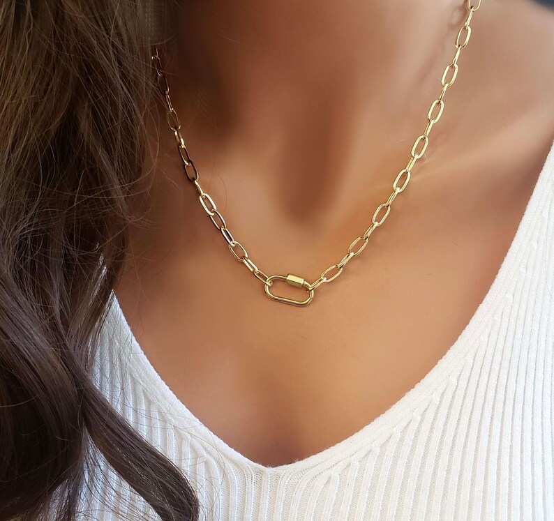 Puede incluir: Un collar de cadena dorada con un cierre ovalado dorado. El collar est&aacute; en un maniqu&iacute; que lleva una camisa blanca.
