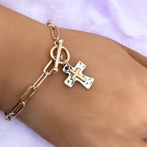 May include: Gold chain bracelet with a toggle clasp and a silver cross charm with a gold center.