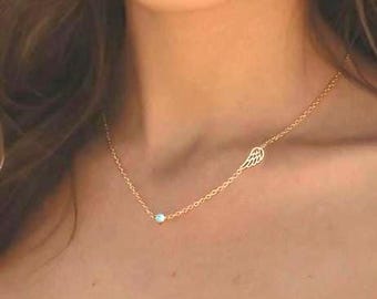May include: A gold-toned chain necklace featuring a small, round, light blue stone charm and a delicate, open-work wing charm. The necklace rests against the neck, showcasing a minimalist design with two distinct charms spaced along the chain.