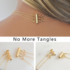 May include: Gold necklace clasp with three strands, designed to prevent tangling. The clasp is a gold-colored bar with three loops for attaching the necklace chains. The text "No More Tangles" is visible below the clasp.