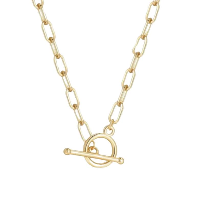May include: A gold-toned necklace featuring a series of elongated oval links connected to a circular toggle clasp with a horizontal bar. The chain has a polished metallic finish and a consistent link design throughout the entire length of the piece.