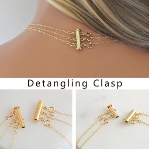 May include: Gold-toned necklace with a multi-strand design, featuring a detangling clasp. The clasp is a vertical bar with multiple loops for attaching the necklace strands. The text "Detangling Clasp" is visible below the image.