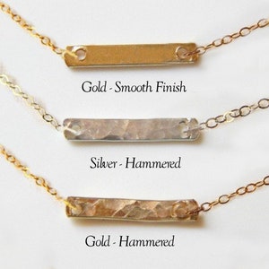 Puede incluir: Tres collares de barra horizontal con cadenas delicadas. El superior es una barra dorada con acabado liso. El medio es una barra plateada con textura martillada. El inferior es una barra dorada con textura martillada. Las etiquetas dicen Gold - Smooth Finish, Silver - Hammered y Gold - Hammered.