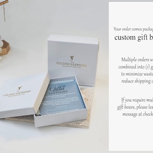 May include: A white square gift box with a gold Gilded Sapphire logo, featuring an open lid and a blue informational card inside. The text on the right reads: Your order comes packaged in our custom gift boxes. Multiple orders will be combined.