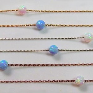 May include: Six delicate necklaces, each featuring a single opal bead in a variety of colours, including white, blue, and iridescent. The necklaces are presented against a white backdrop.