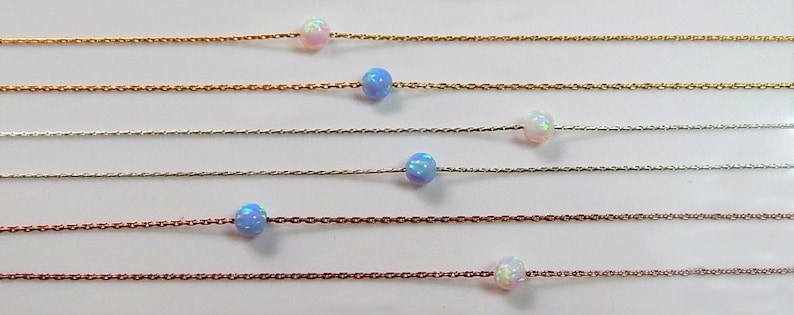 May include: Six delicate necklaces, each featuring a single opal bead in a variety of colours, including white, blue, and iridescent. The necklaces are presented against a white backdrop.