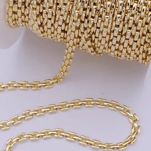 May include: A spool of gold-colored chain with a rectangular link design. The chain is shown in a close-up view, highlighting the intricate details of the links and the metallic sheen. The chain is likely used for jewelry making or crafting.