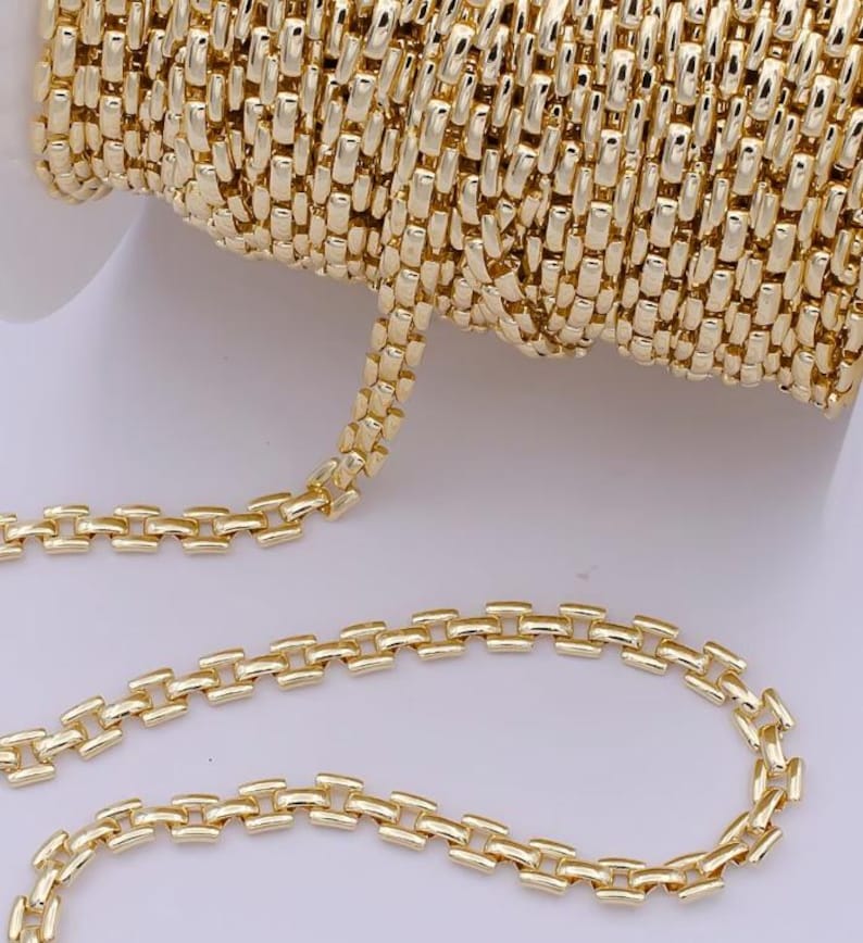 May include: A spool of gold-colored chain with a rectangular link design. The chain is shown in a close-up view, highlighting the intricate details of the links and the metallic sheen. The chain is likely used for jewelry making or crafting.