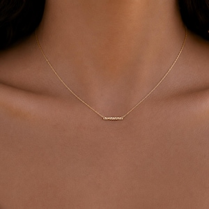 Puede incluir: Un delicado collar de cadena dorada que presenta un peque&ntilde;o colgante de barra rectangular horizontal con una superficie texturizada y brillante. La fina cadena dorada pulida se conecta a cada extremo de la barra, creando una joya sencilla.