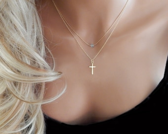 May include: A gold chain necklace with a small cross pendant and a single, small, round, clear stone pendant.