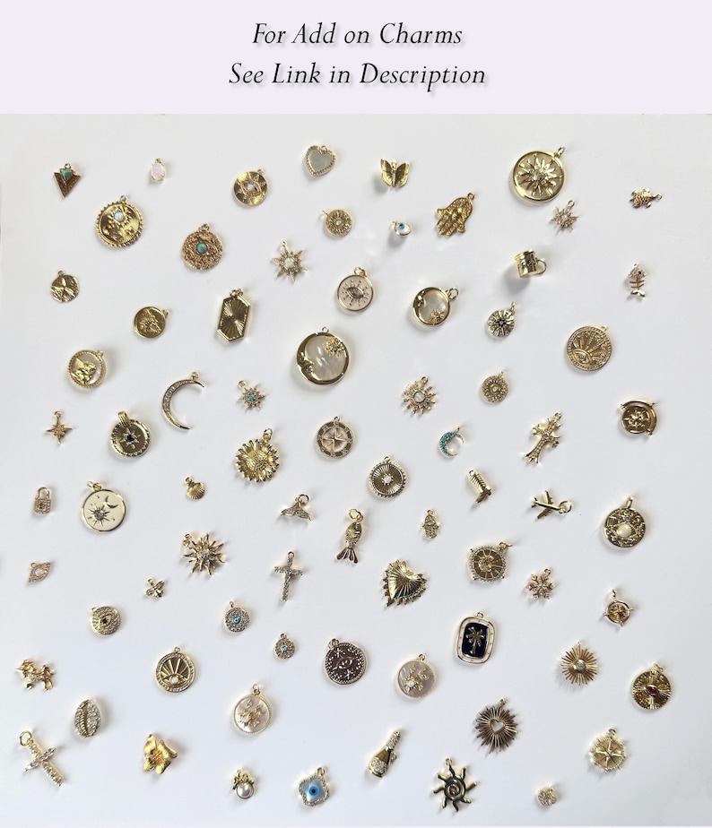 May include: A collection of gold-toned charms in various shapes and sizes, including suns, moons, crosses, and hearts. The charms are displayed on a white surface. Text at the top reads "For Add on Charms See Link in Description."