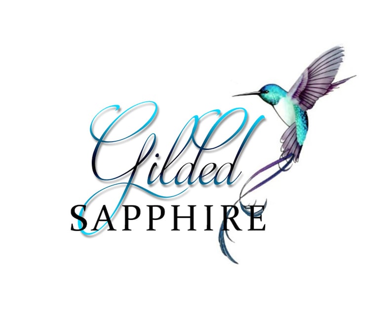 K&ouml;nnte beinhalten: Ein Logo mit dem Text "Gilded Sapphire" in einer blauen und schwarzen Schriftart. Ein blauer und violetter Kolibri mit einem langen, geschwungenen Schwanz fliegt &uuml;ber dem Text.