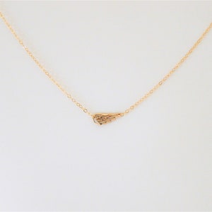 Może przedstawiać: Złoty naszyjnik z delikatnym, małym zawieszką w kształcie skrzydła.