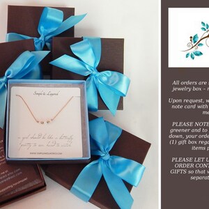 May include: Several brown gift boxes tied with light blue satin ribbons. One box is open, revealing a delicate gold necklace with small, round charms on a white card. The card has text that reads "Simple & Layered".