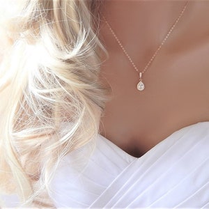 May include: A delicate rose gold necklace with a pear-shaped crystal pendant. The pendant is surrounded by smaller crystals, creating a sparkling halo effect.